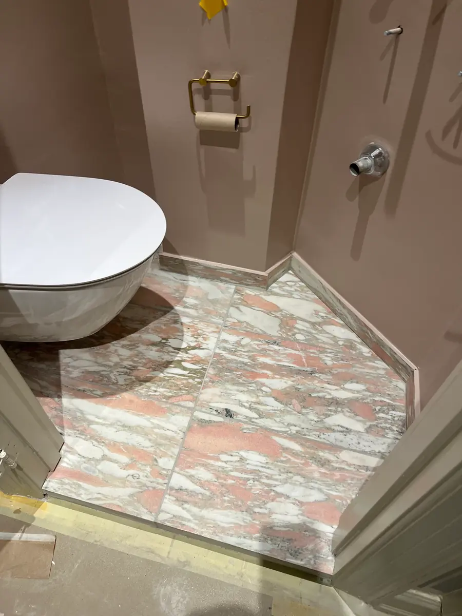 Færdig toiletkrog med rosa marmorgulv, støvet lilla vægge, væghængt toilet og messingholder