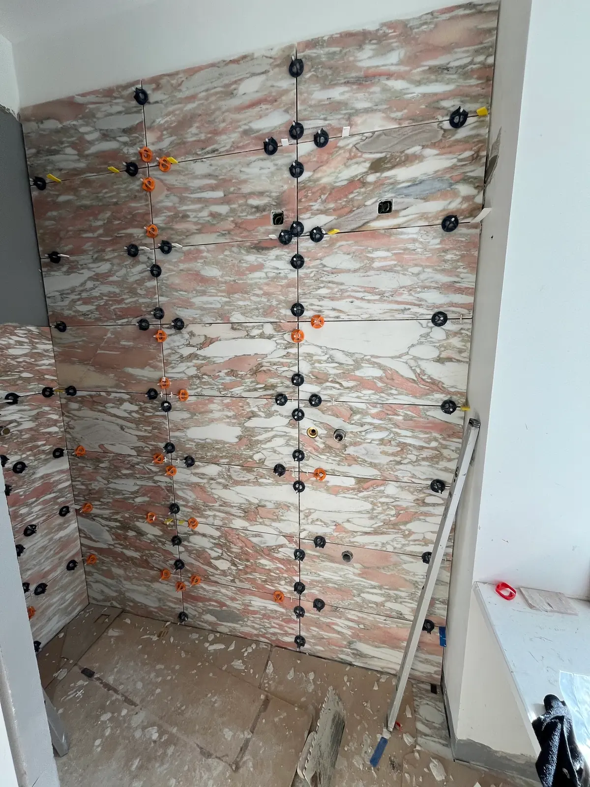 Hel væg i rosa marmorfliser med nivelleringsklips i alle fuger og udsparinger til indbygningsarmatur